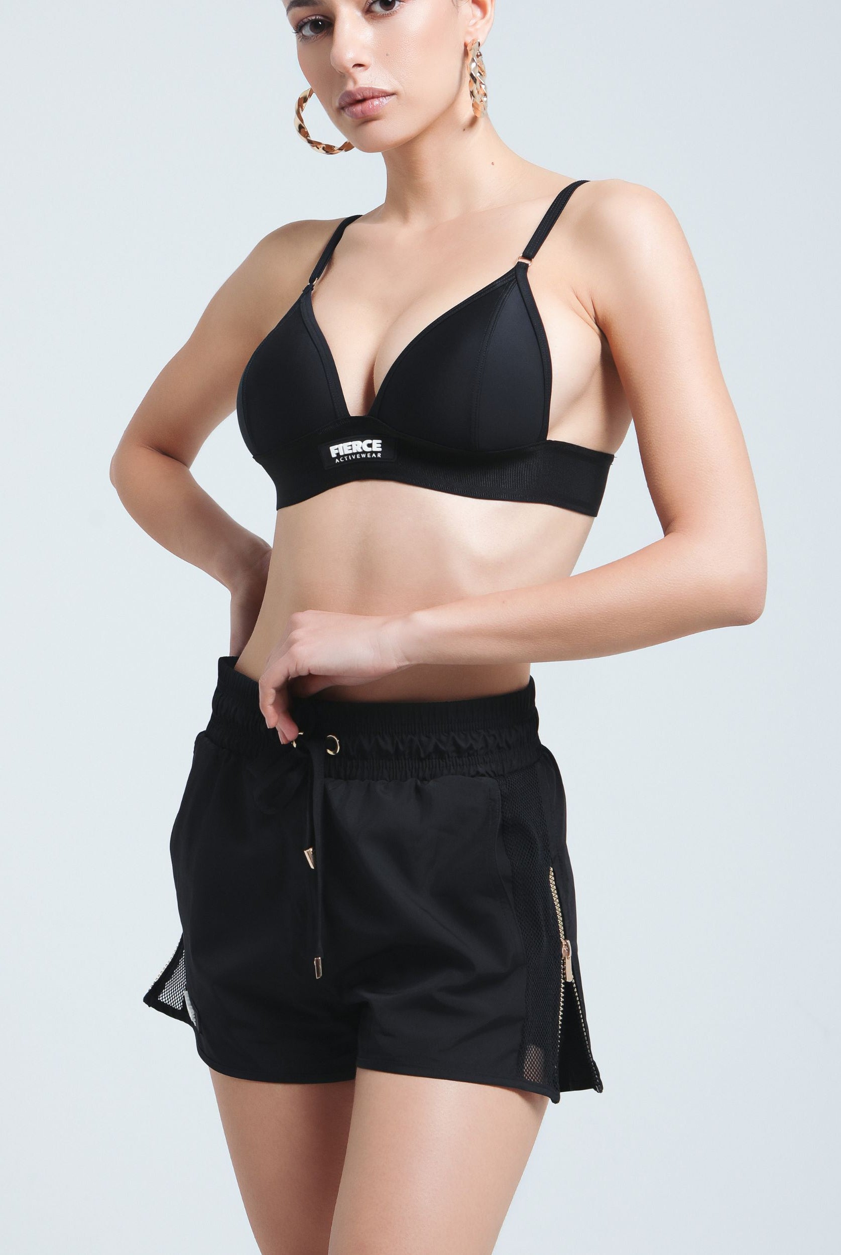 Front view of a woman wearing Fierce Activewear's black Aero running shorts with gold zip details, paired with the black Serena triangle bikini top