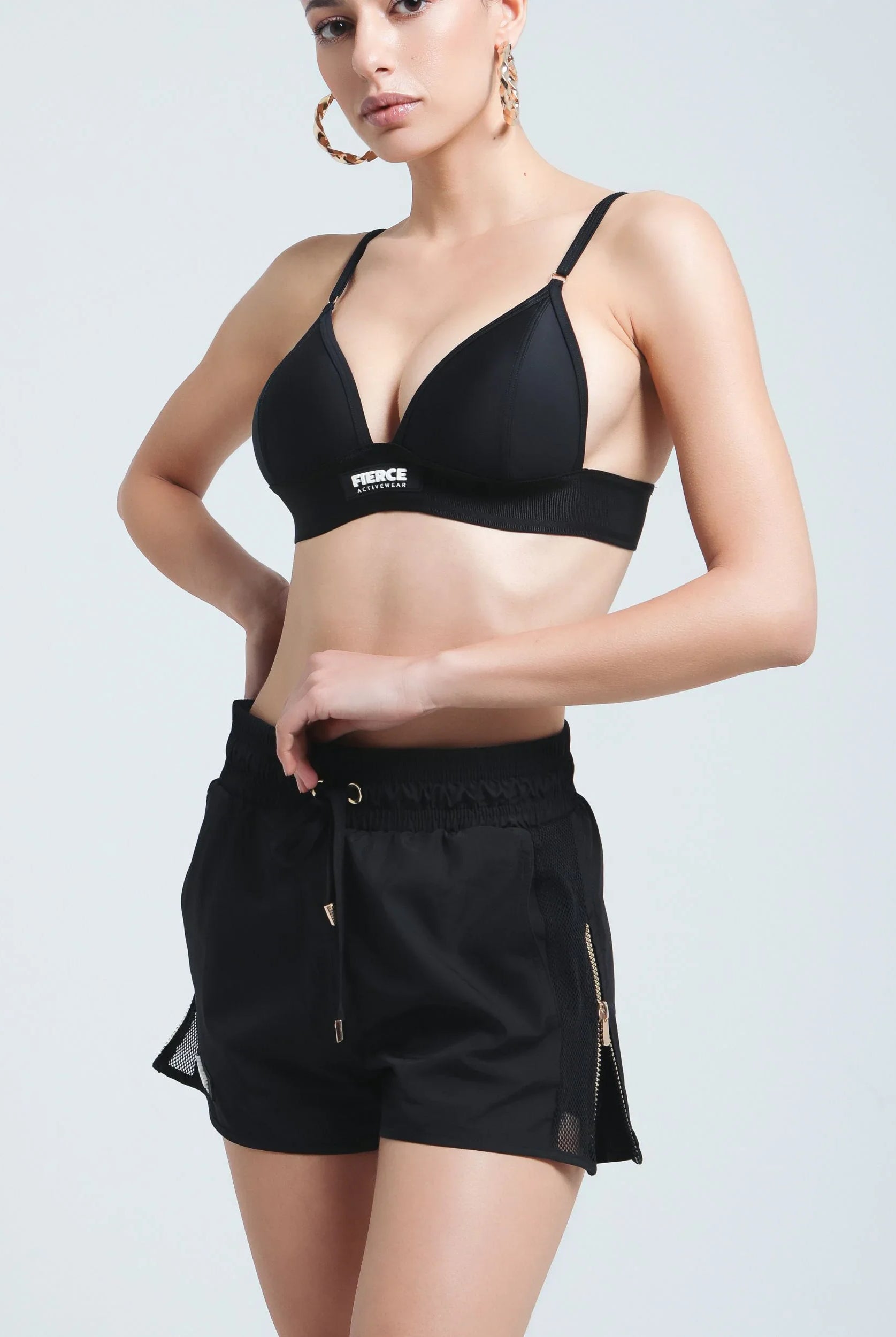 Front view of a woman wearing Fierce Activewear's black Aero running shorts with gold zip details, paired with the black Serena triangle bikini top