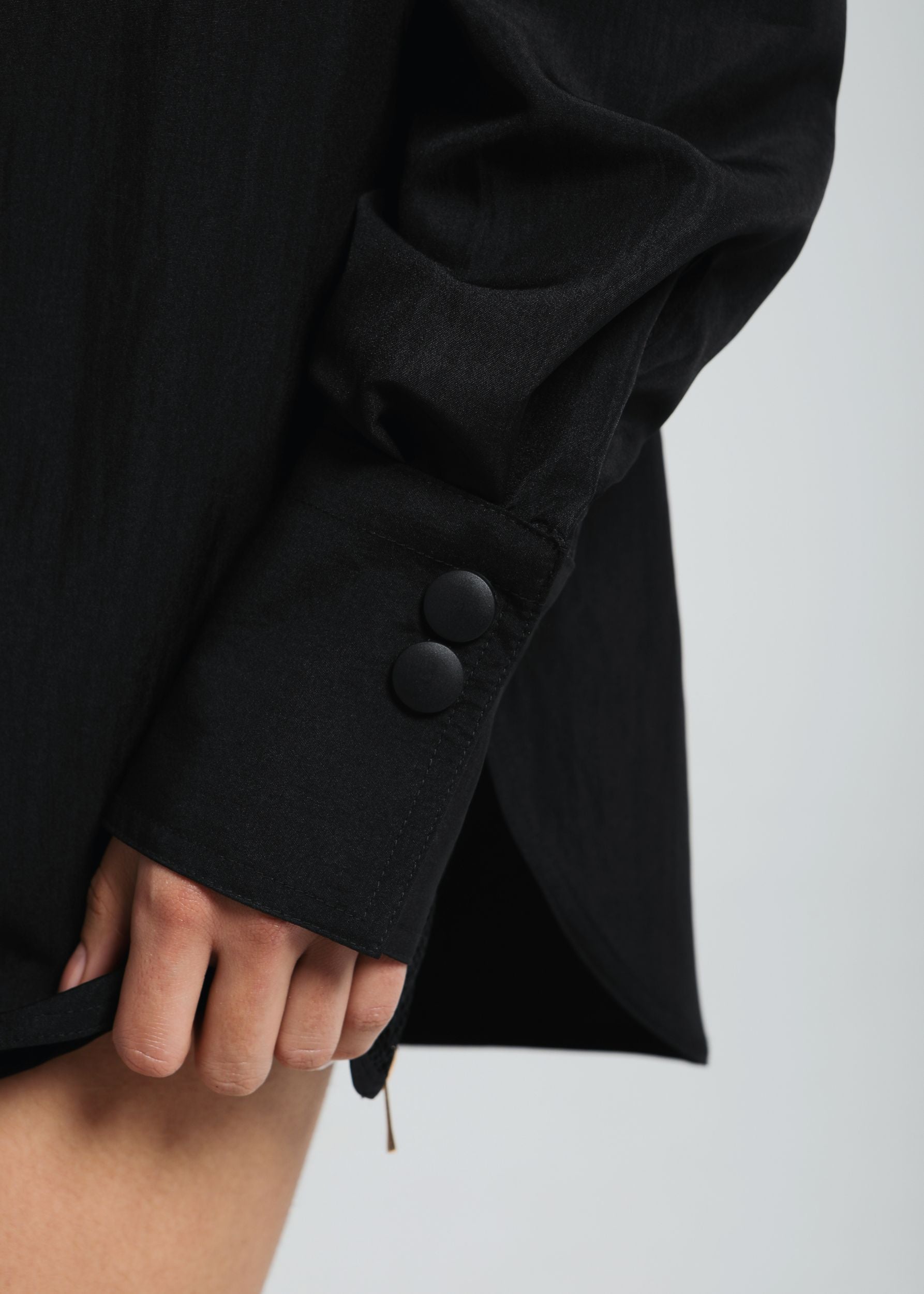 Close-up of Fierce's model hand and black shirt cuff with button detail and curved hem – minimal and textured design focus