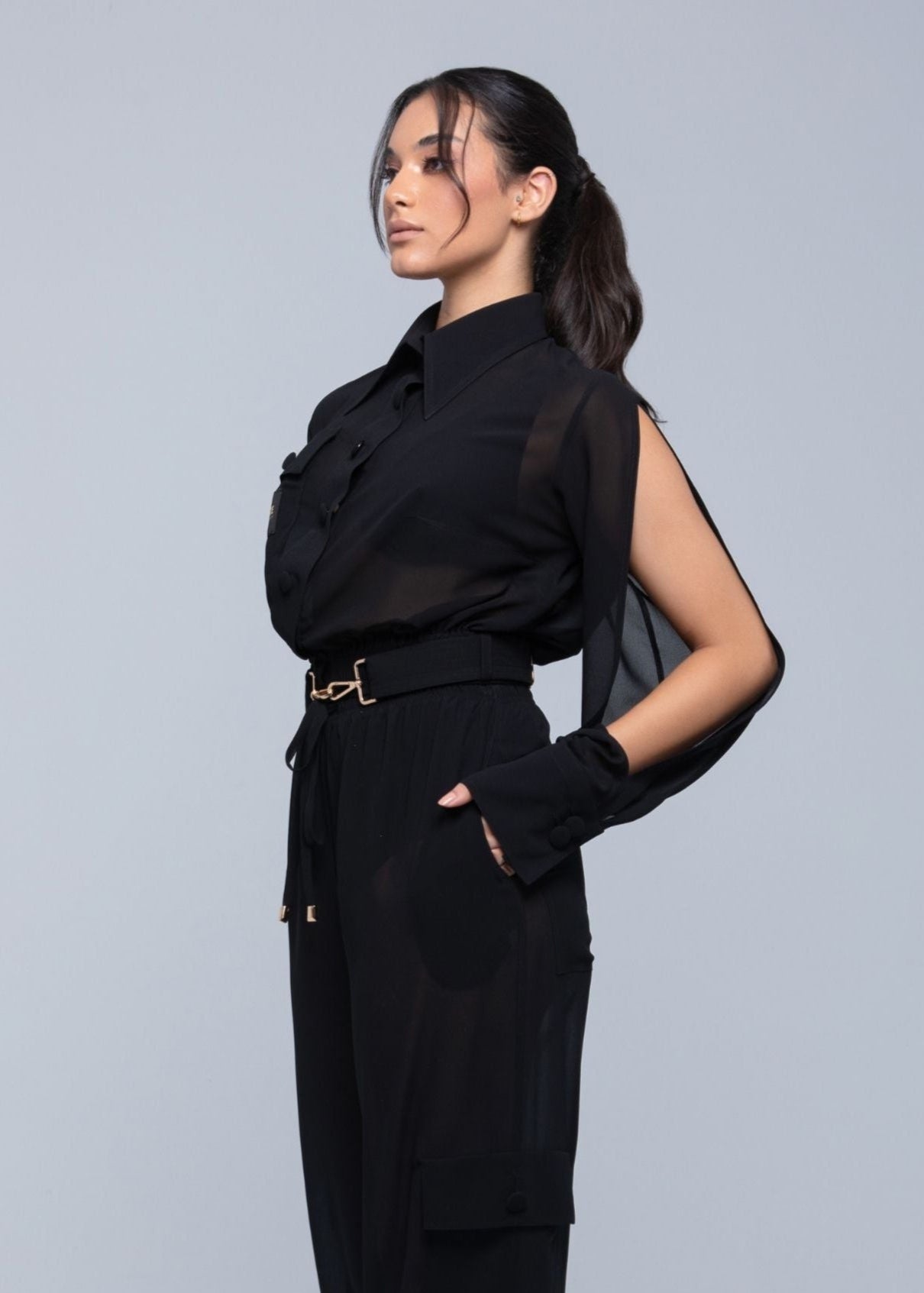 This image features a stylish and modern Fierce sheer jacket, presented in a classic black color. The jacket is designed with a V-neckline and includes unique gold-tone hardware at the neck and mid-back, adding a touch of elegance.