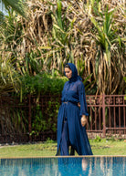 Woman in a Fierce blue dress standing by a pool with greenery in the background