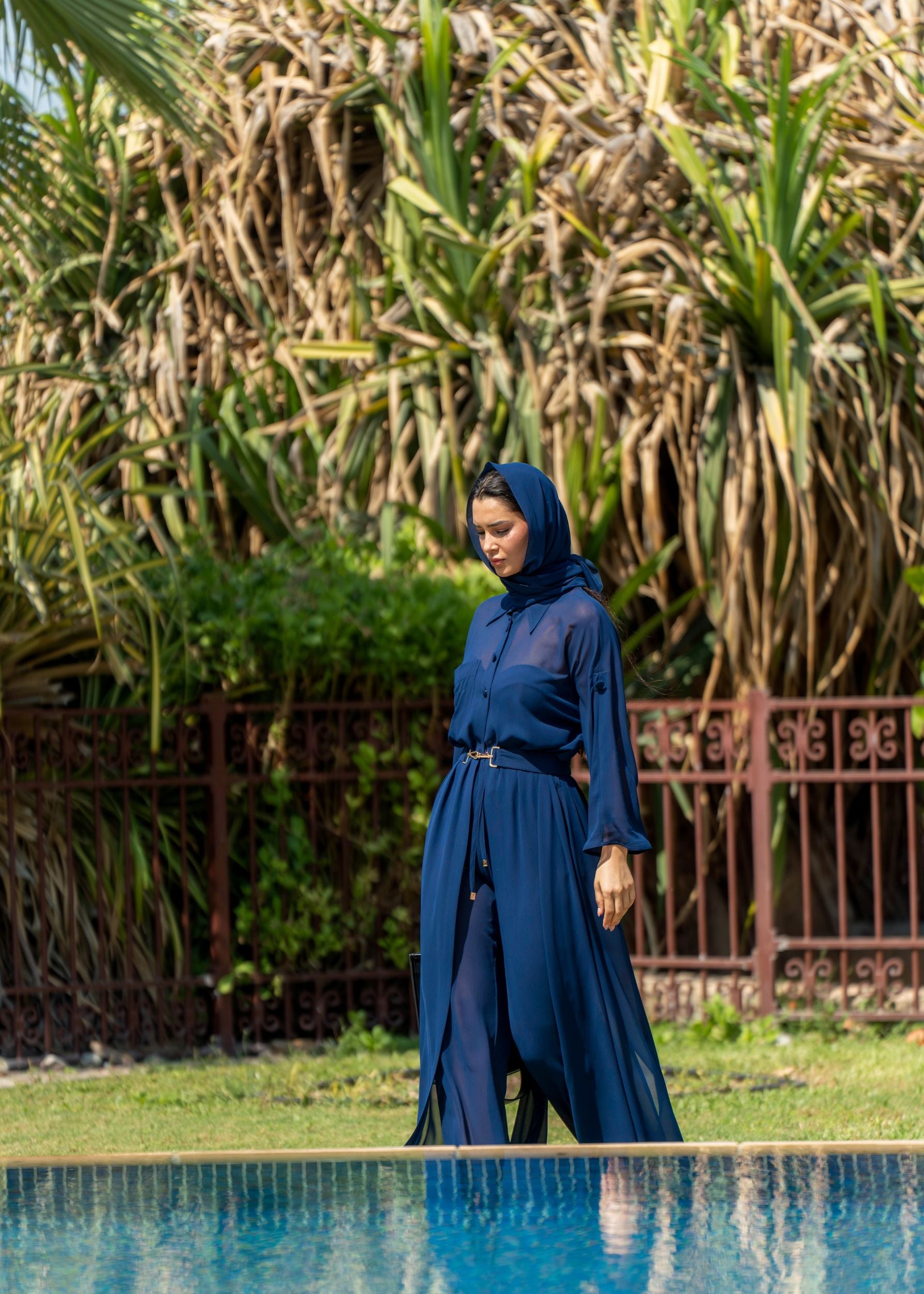 Woman in a Fierce blue dress standing by a pool with greenery in the background