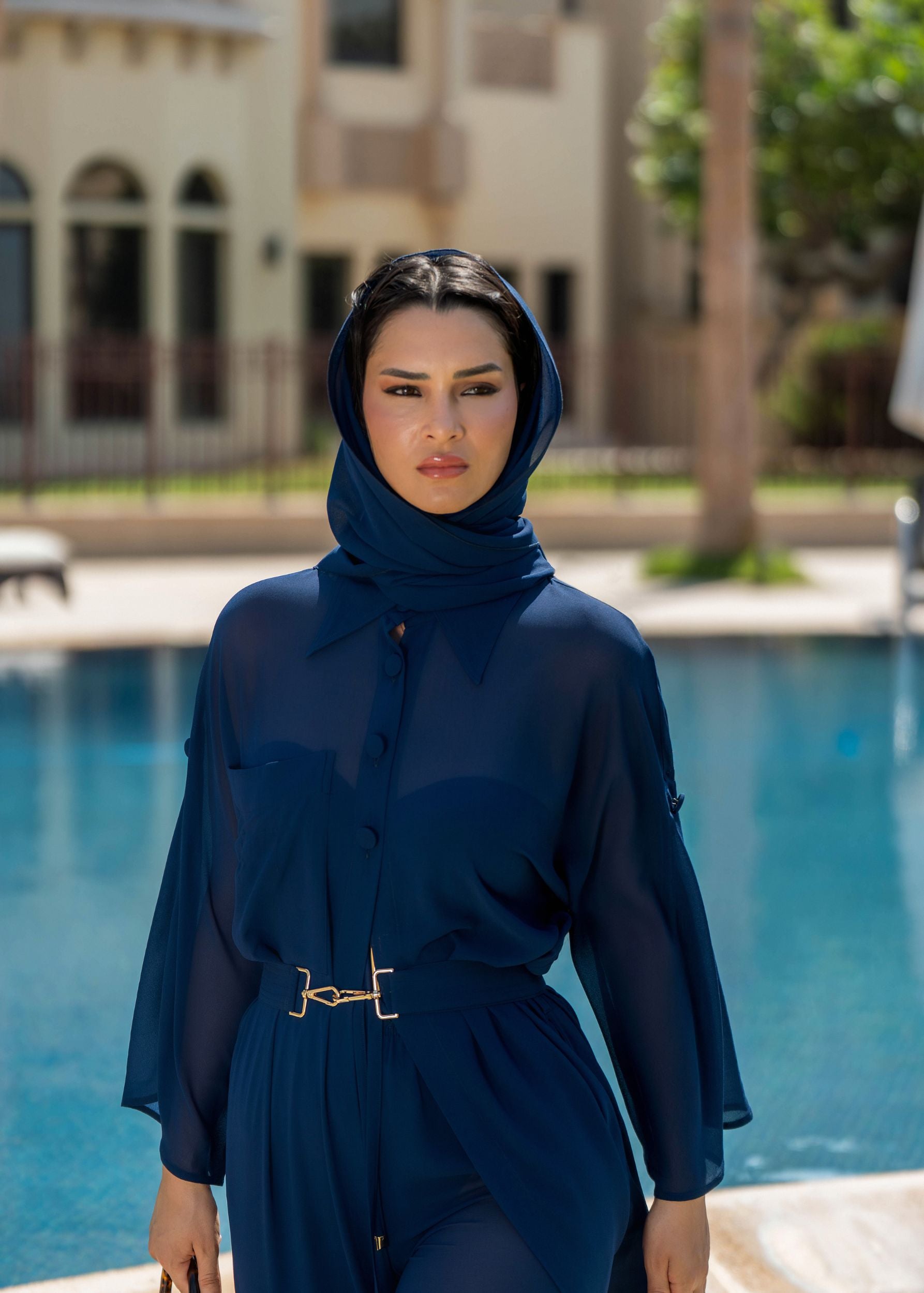 Woman in a Fierce blue outfit standing by a pool with a blurred building and palm tree in the background