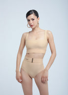 Woman wearing a Fierce beige swimsuit with a belt on a light gray background