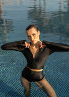 Woman in a black Fierce swimsuit standing in a pool with reflections on the water.