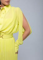 Close-up of neon yellow pleated Fierce skirt with a gold buckle belt, paired with a matching slit-sleeve button-up blouse.