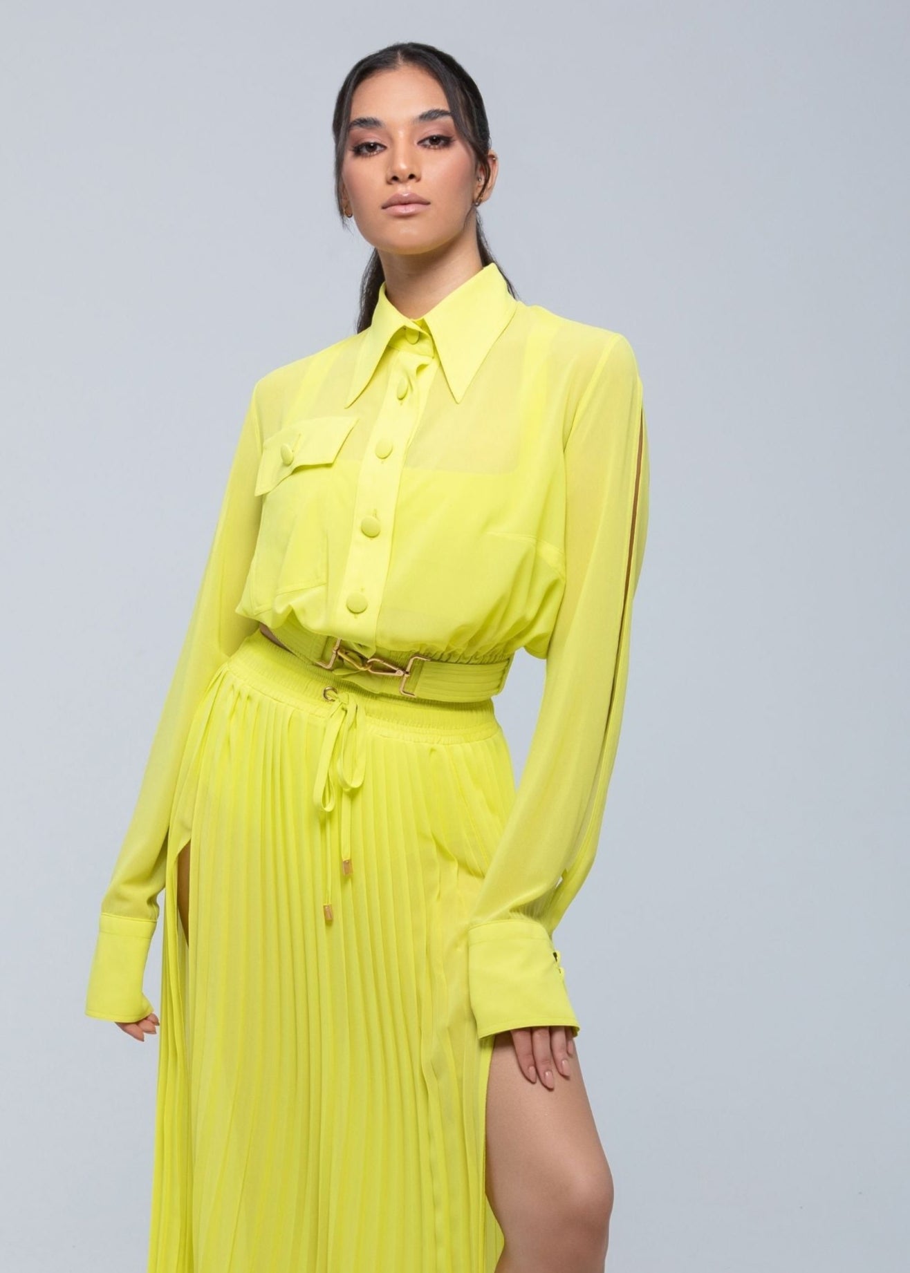 Model wearing a vibrant neon yellow Fierce long-sleeve shirt paired with a matching pleated skirt featuring a thigh-high slit and belted waist, creating a bold monochrome fashion look.