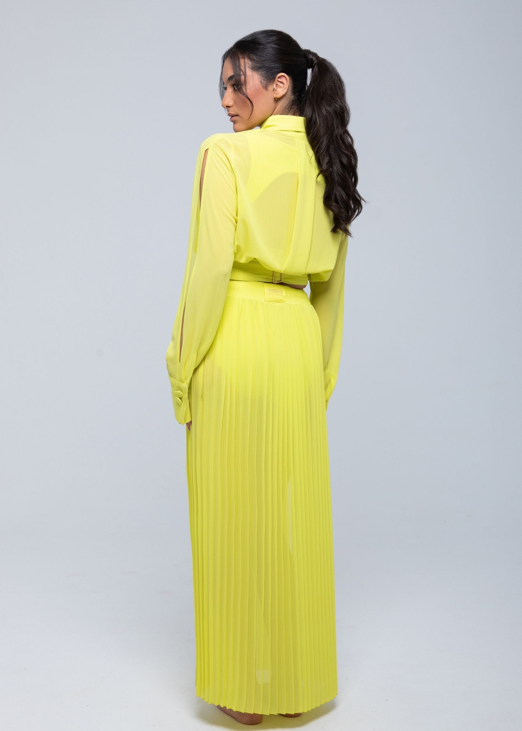 Back view of a model wearing a neon yellow Fierce long-sleeve shirt paired with a matching pleated maxi skirt, showcasing a belted waist and a sleek monochrome design.