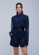 Model facing forward, wearing a Fierce sheer navy blue long-sleeve shirt with buttoned front and chest pocket, paired with high-waisted navy shorts featuring a drawstring waist and decorative belt detail.