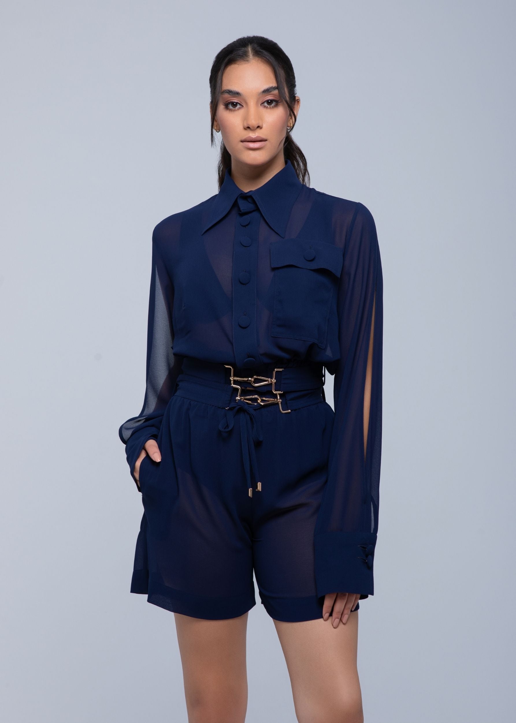 Model facing forward, wearing a Fierce sheer navy blue long-sleeve shirt with buttoned front and chest pocket, paired with high-waisted navy shorts featuring a drawstring waist and decorative belt detail.