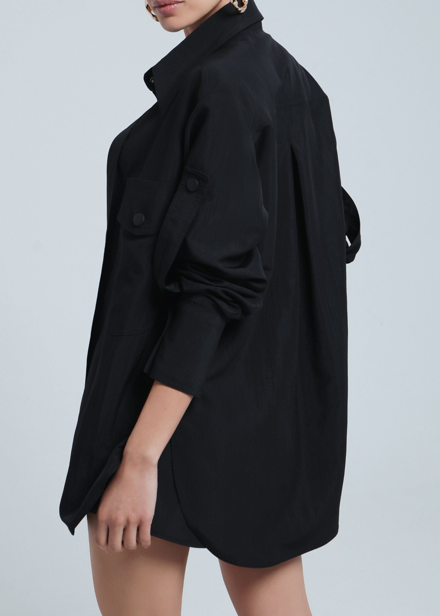 Back-side view of a model in a relaxed-fit black shirt dress with rolled-up sleeves, showcasing the oversized silhouette