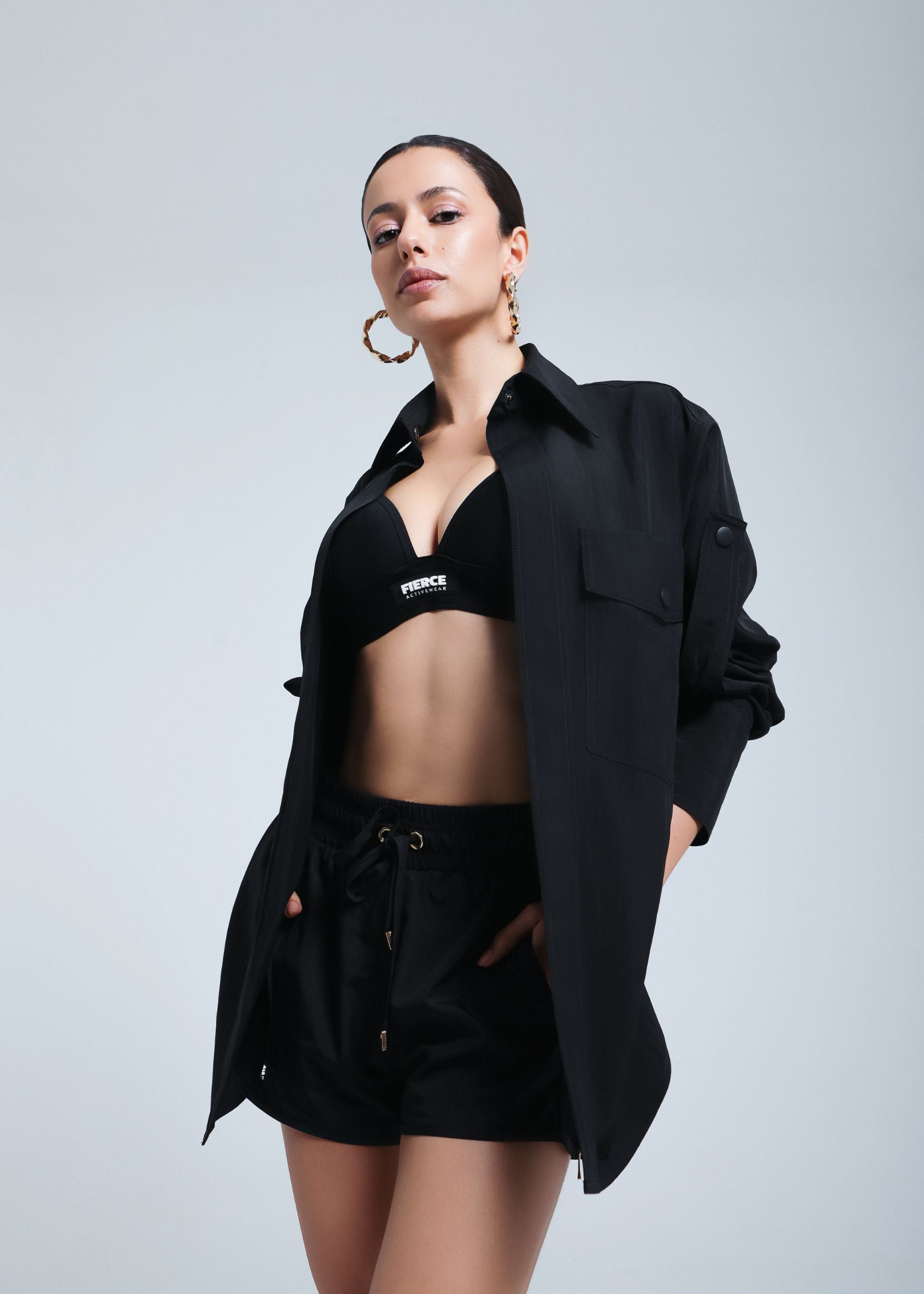 Model wearing a black bralette and drawstring shorts layered with an Fierce oversized black shirt, posing confidently with hands in pockets