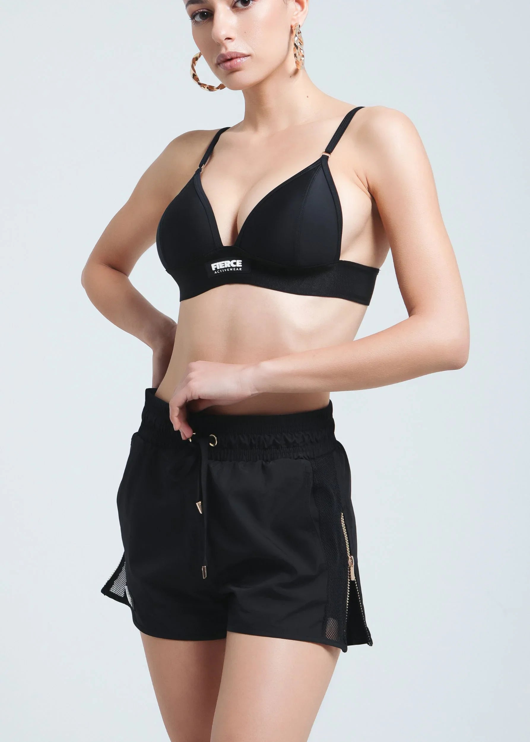 Front view of a woman wearing Fierce Activewear's black Aero running shorts with gold zip details, paired with the black Serena triangle bikini top