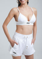 Woman wearing Fierce Activewear's white Aero running shorts paired with a matching white triangle top, featuring zippered pockets, elastic waistband, and gold accents