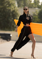 Woman posing on a road wearing black Fierce cargo pants and a black top with a crop, carrying an orange surfboard.