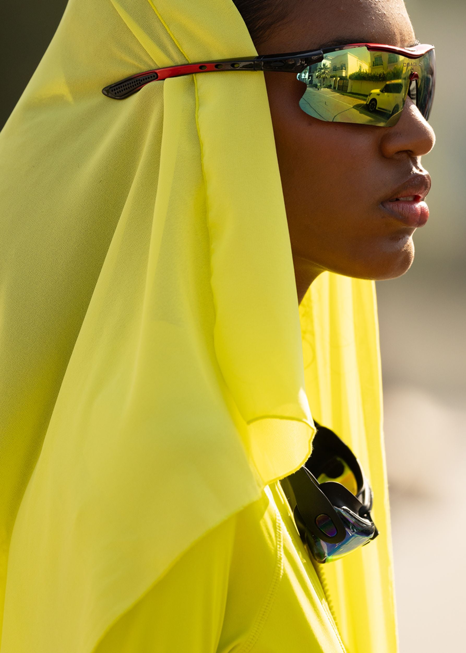Person wearing a yellow Fierce headscarf and reflective sunglasses with a blurred background